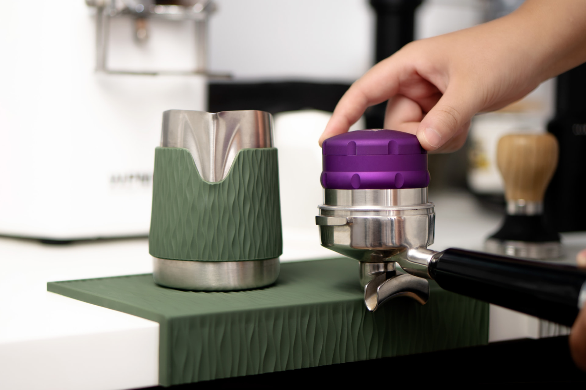 A green Airflow milk jug with a textured silicone band and a purple distributor on an espresso portafilter.