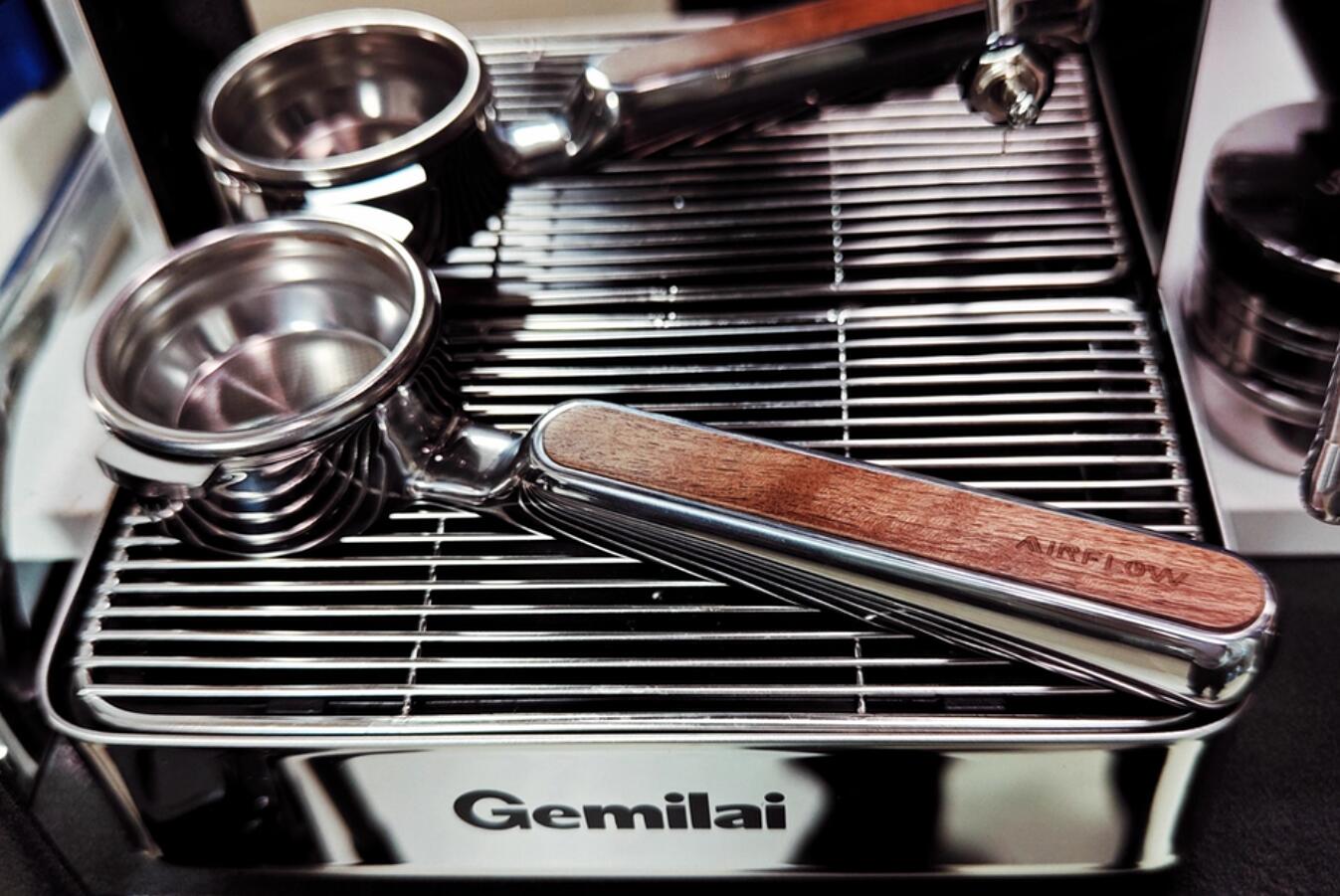 Airflow flat mirror portafilter resting on an espresso machine drip tray beside two spouted portafilters